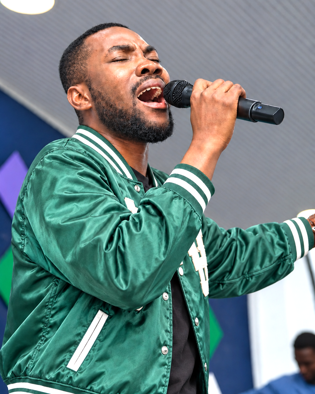 Schadrac Loman en bomber vert, chantant au microphone